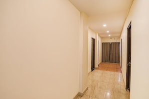A narrow hallway with a tiled floor, plain walls, and doors leading to rooms. - Fabexpress Park View (Hingna)