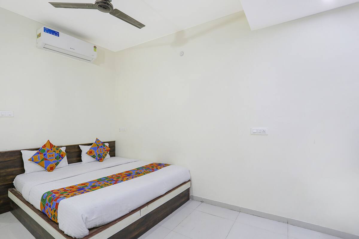 A bedroom with a bed, a ceiling fan, an air conditioner, and a white wall.