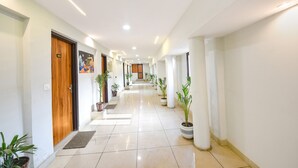 A hotel hallway with a wooden door labeled '103', potted plants, and a tiled floor.