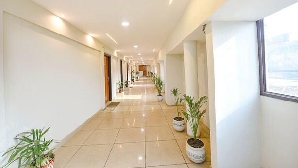 A long, well-lit hallway with potted plants and a view of the outside through a window.