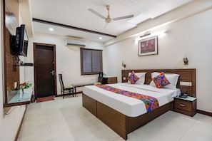 A hotel room with a bed, bedside table, desk, chair, TV, and artwork on the wall. - Fabhotel Amman (Agra)