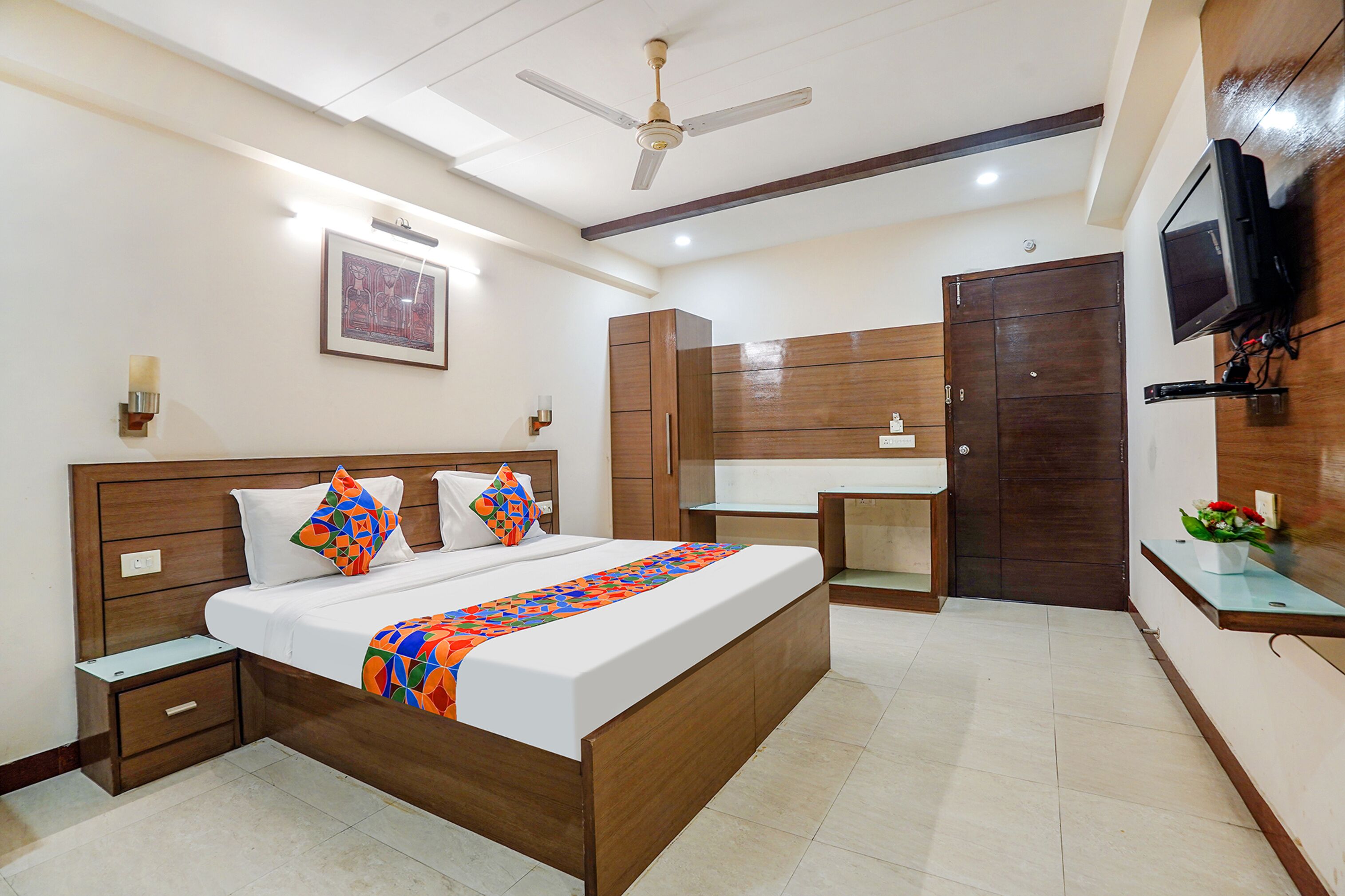 A hotel room with a bed, bedside tables, a wardrobe, a mirror, a TV, and a ceiling fan.