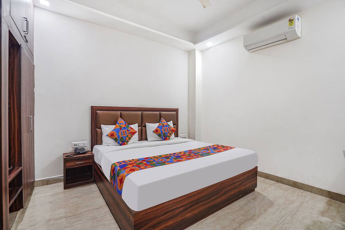 A bedroom with a wooden bed frame, a bedside table with a phone, and a wall-mounted air conditioner.