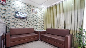 A living room with two brown leather sofas, a small white table, a flat-screen TV mounted on the wall, patterned wallpaper, and a green curtain.
