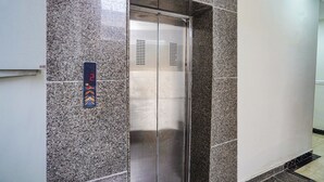 An elevator with a metallic finish, set in a hallway with granite tiles.