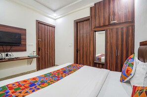 A hotel room with a bed, a TV mounted on the wall, wooden wardrobes, and a colorful runner on the floor. - Fabhotel Golden Grand (Agra)
