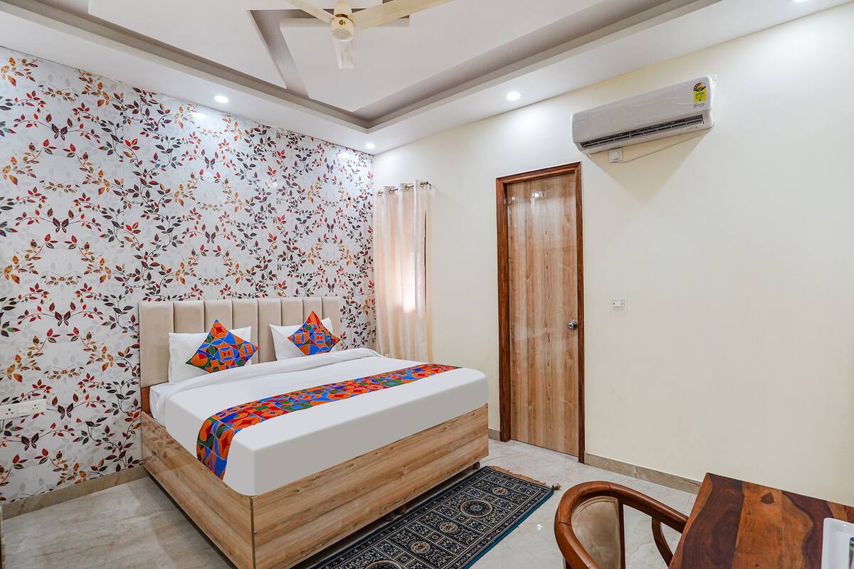 A bedroom with a bed, a wooden headboard, a patterned rug, a wooden table, and a ceiling fan.