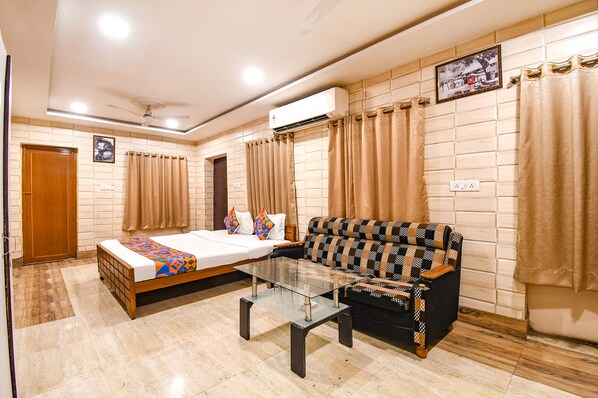 A hotel room with a bed, sofa, glass coffee table, and an air conditioning unit.
