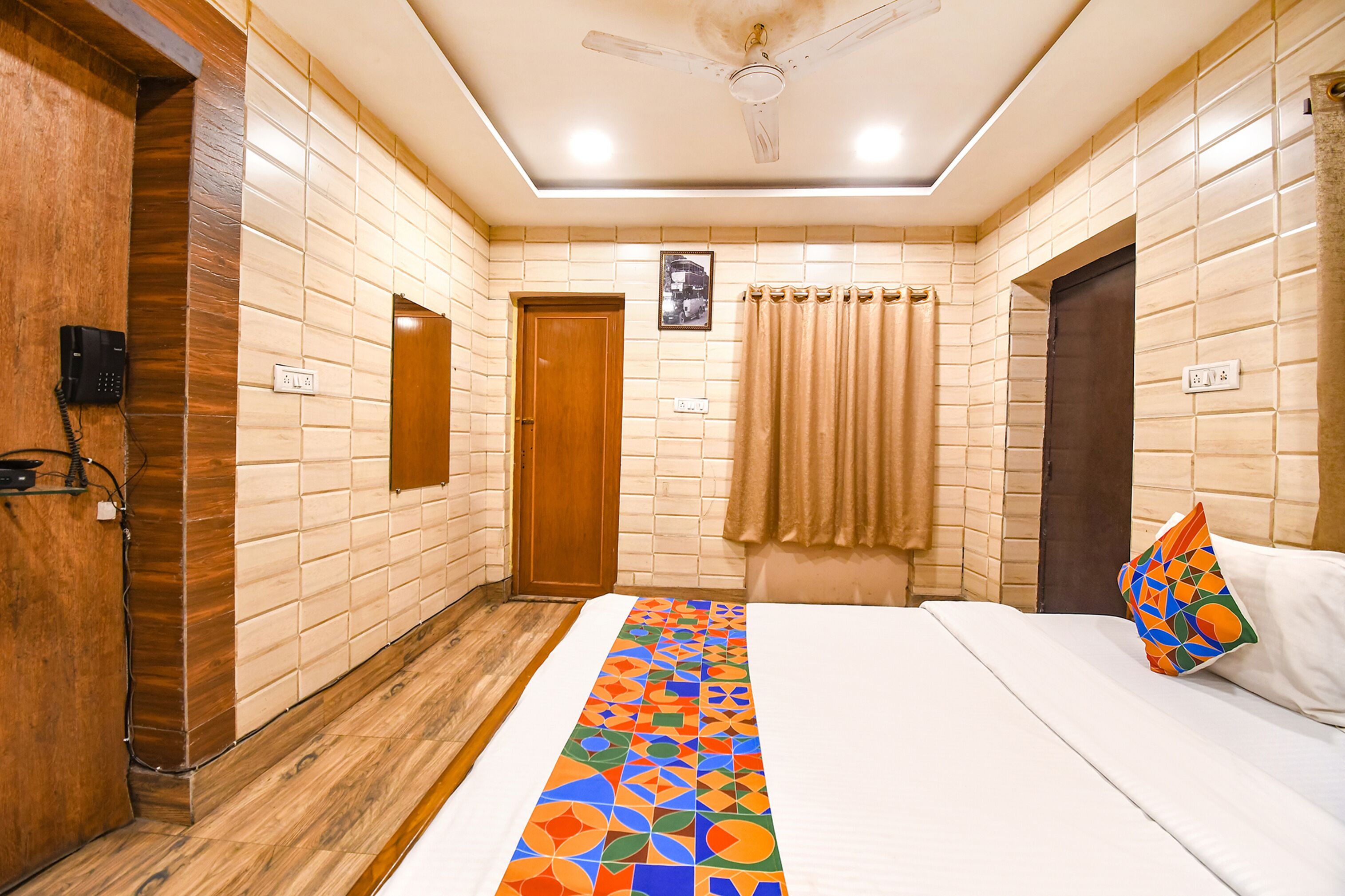 A hotel room with a bed, a ceiling fan, a wooden door, and a wall with a geometric patterned runner.