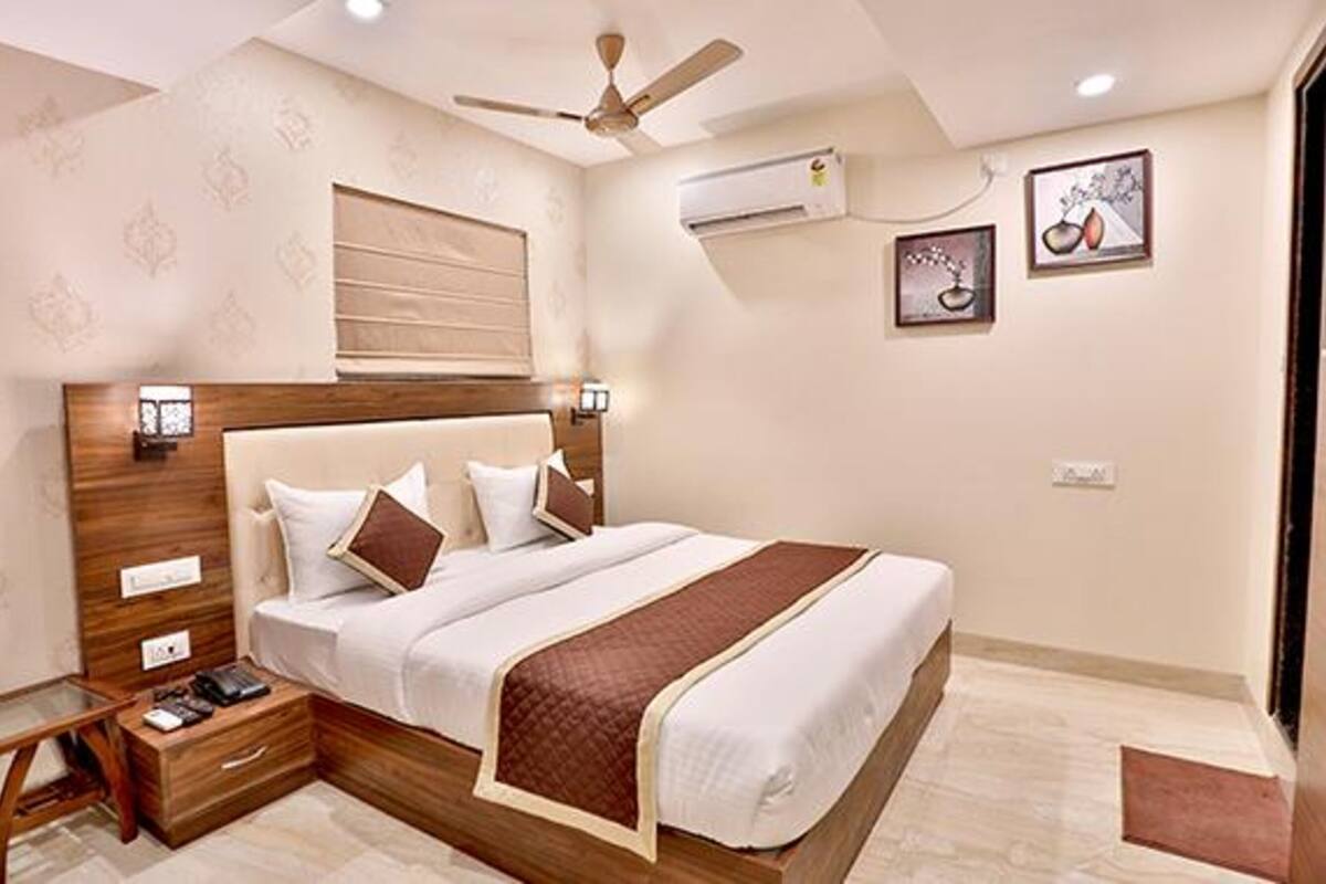 A neatly arranged hotel room with a large bed, bedside tables, a ceiling fan, and wall-mounted air conditioning.