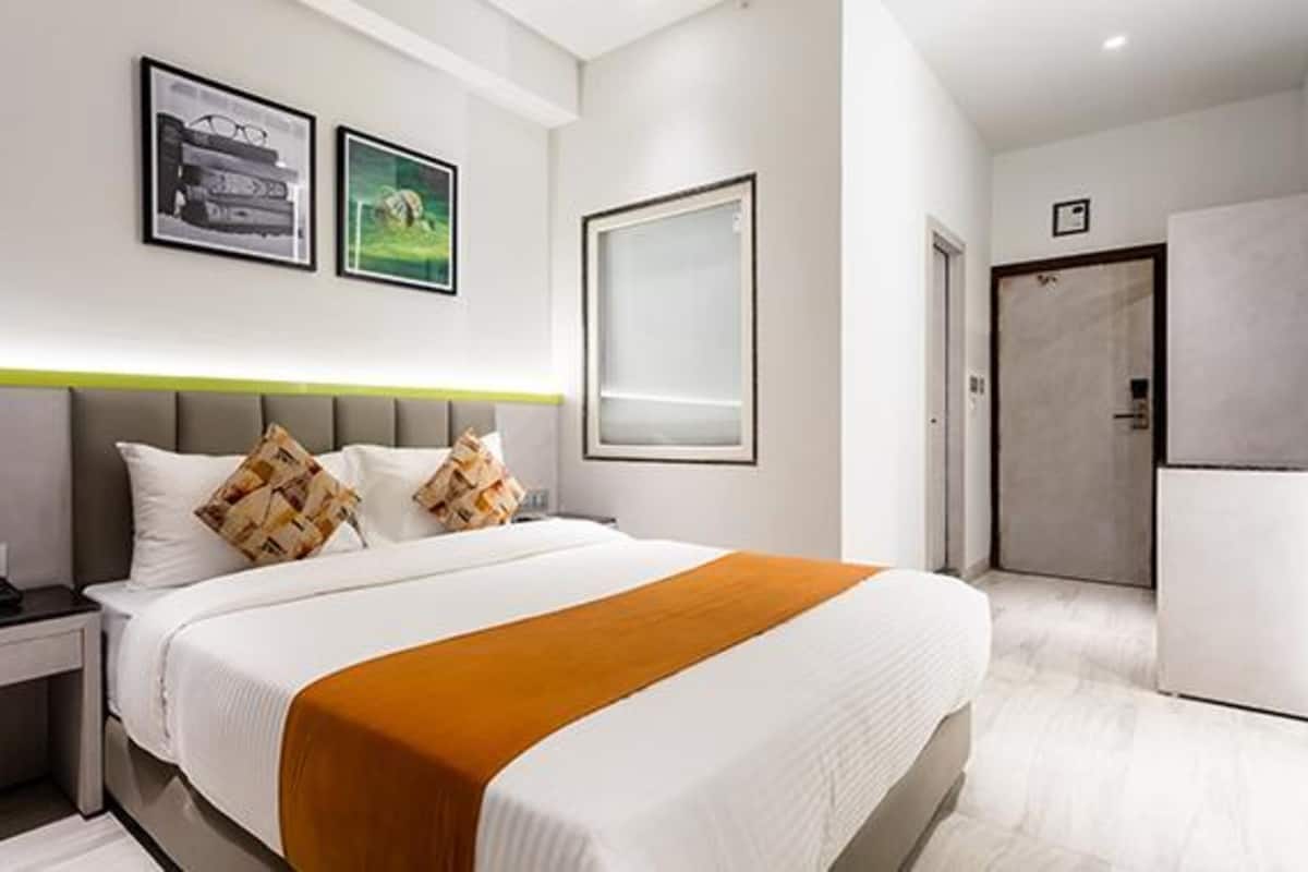 Een moderne hotelkamer met een groot bed, een nachtkastje, een bureau en een garderobe. Er hangen afbeeldingen in lijsten aan de muur en er is een groot raam.
