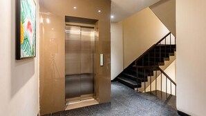 An elevator with a metallic finish, a staircase with black railings, and a wall-mounted artwork. - FabHotel Orange Oasis (Bhopal)