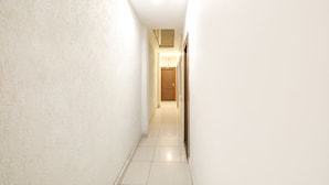 Un pasillo estrecho, bien iluminado, con paredes blancas y piso de baldosas, que conduce a una puerta de madera al final.