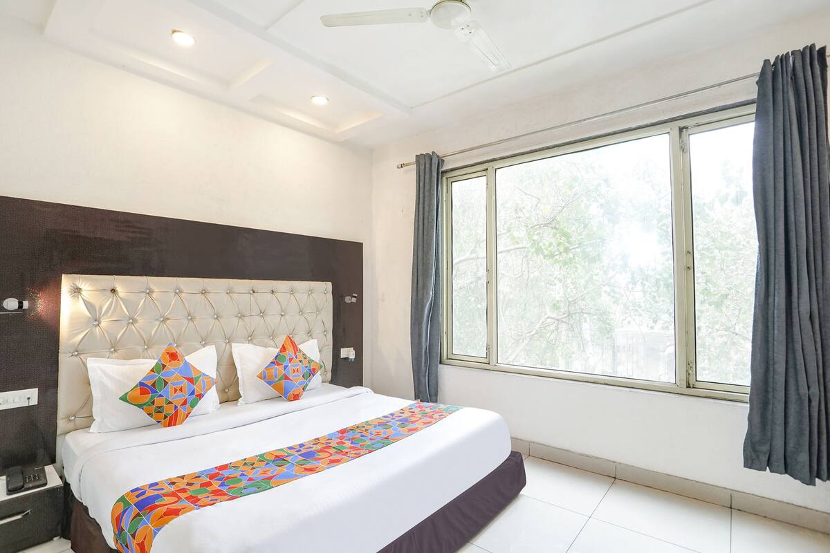 Una habitación de hotel con una cama grande, un cabecero tapizado, una ventana con cortinas y un ventilador de techo.