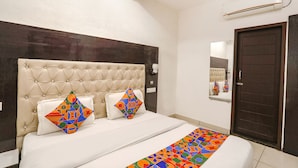 Habitación de hotel con cabecera capitonada, un espejo grande, una puerta de madera oscura y un corredor de cama con un estampado geométrico colorido.