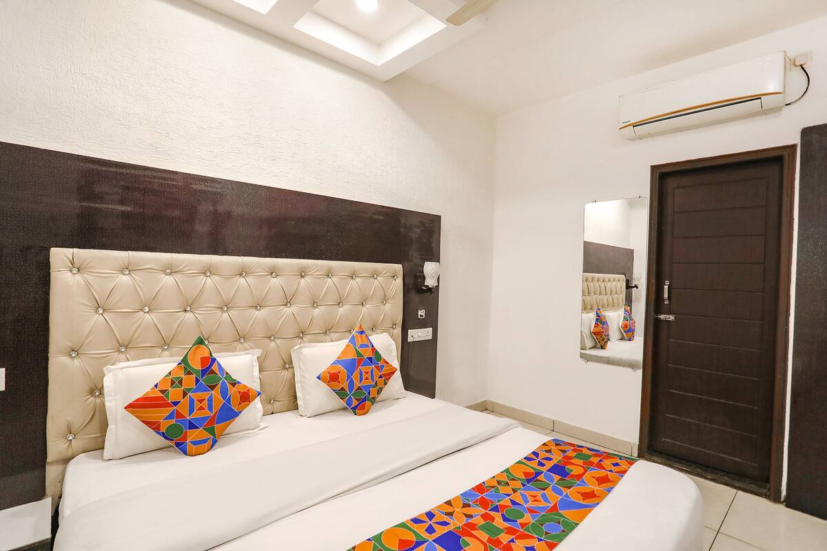 Habitación de hotel con cabecera capitonada, un espejo grande, una puerta de madera oscura y un corredor de cama con un estampado geométrico colorido.