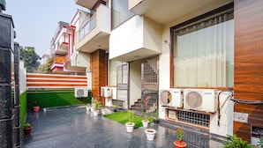 A modern building with a green lawn, potted plants, and air conditioning units. - Fabhotel Apple Pie (Noida)