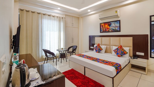 A hotel room with a bed, a desk, a chair, a small table, a red rug, and a ceiling fan. - Fabhotel Apple Pie (Noida)
