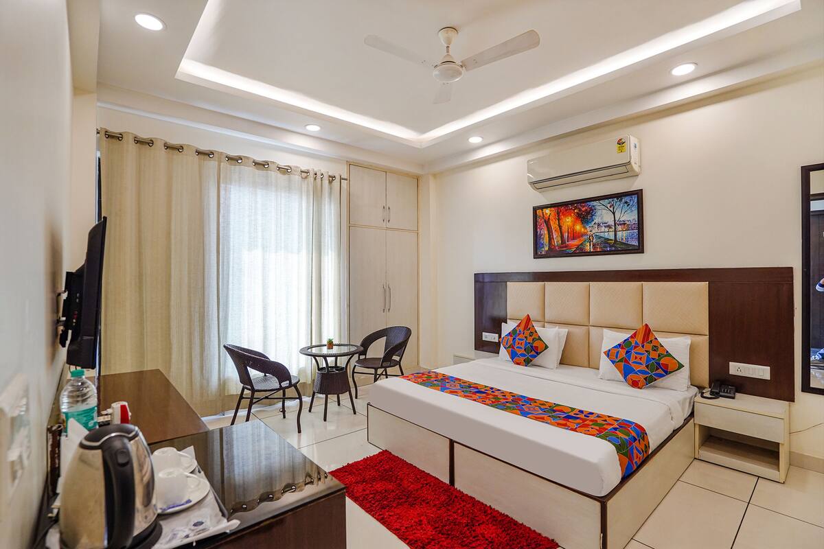 A hotel room with a bed, a desk, a chair, a small table, a red rug, and a ceiling fan.