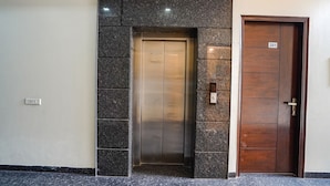 An elevator with a metallic finish, a wooden door with the number 201, and a wall with a granite-like texture. - Fabhotel Apple Pie (Noida)