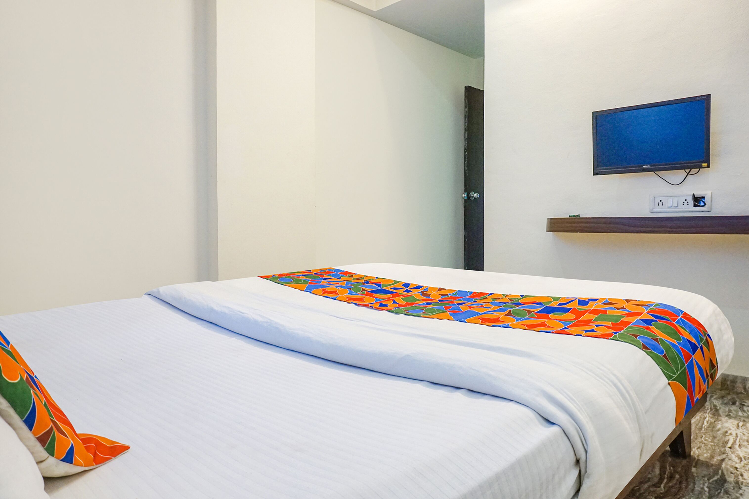 Una camera d'hotel con un letto, una televisione fissata al muro e una presa di corrente sul comodino.