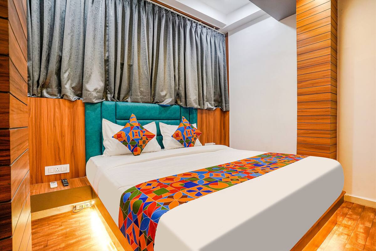 A neatly made bed with a colorful geometric-patterned bedspread, a teal upholstered headboard, and a grey curtain.