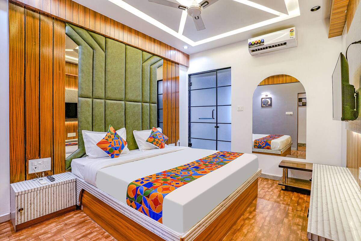 A modern hotel room with a large bed, a wooden headboard, a built-in wardrobe, a bedside table, and a small desk.
