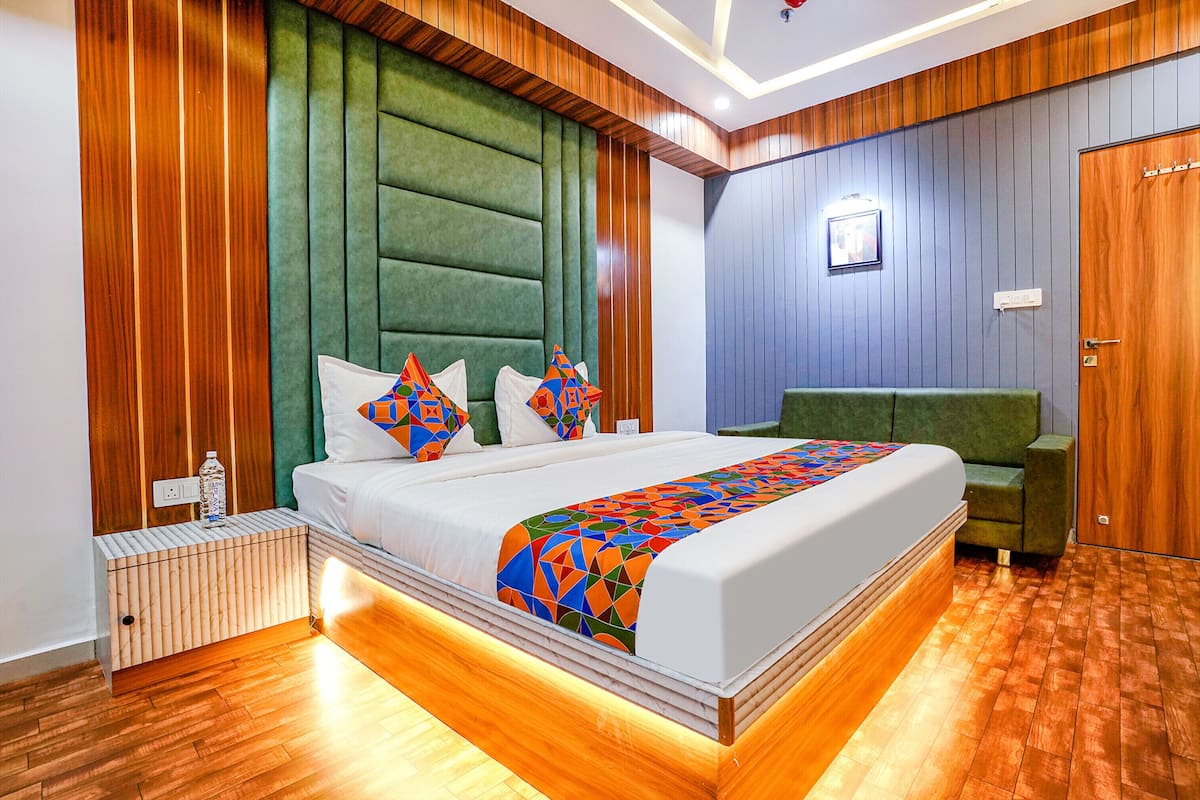 A modern hotel room with a large bed, green upholstered headboard, wooden panel walls, and a green armchair.