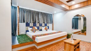 A modern bedroom with a wooden headboard, a large mirror, and a small wooden table. - Fabhotel Max (Vadodara)