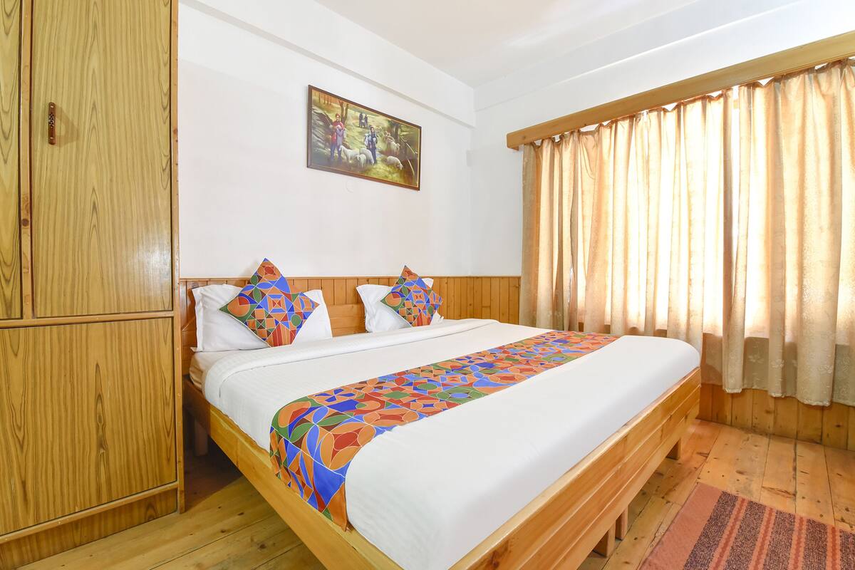 A wooden bed with a colorful bedspread, a painting on the wall, and a window with curtains.