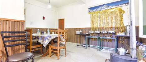 Un comedor con sillas de madera, una mesa con mantel y una mesa de buffet con recipientes de comida.