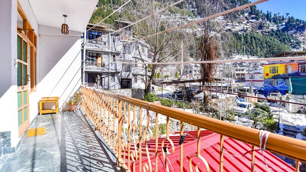 A balcony with a red floor, a white wall, and a view of a snowy mountain and buildings. - Fabhotel Elavali Valley (Manali)