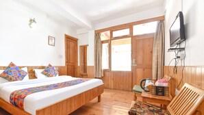 A wooden-paneled room with a bed, a chair, a television, and a window with curtains. - Fabhotel Elavali Valley (Manali)