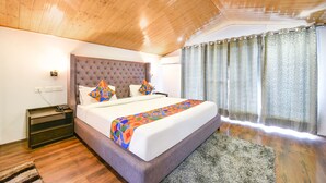 Une chambre à coucher avec un plafond en bois, un grand lit doté d’une tête de lit capitonnée, une couvre-lit à motifs et une fenêtre avec des rideaux.