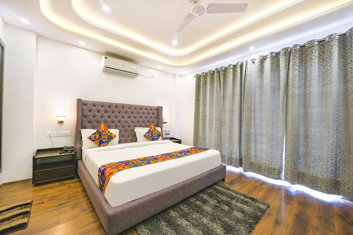 A modern hotel room with a large bed, a ceiling fan, an air conditioning unit, and a window with curtains.