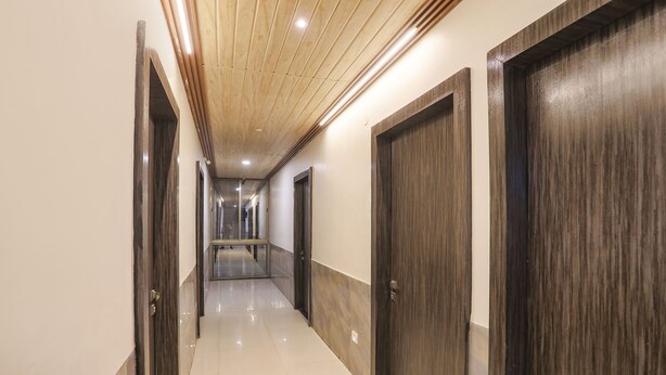 A corridor with wooden doors, a tiled floor, and a wooden ceiling with recessed lighting. - Fabhotel Green Valley I (Dindori)