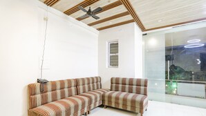 A modern living room with a sectional sofa, a ceiling fan, and a large window with a view. - Fabhotel Green Valley I (Dindori)