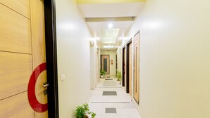 A hallway with a wooden door on the left, a potted plant on the right, and a tiled floor with a central walkway. - Fabhotel Prime Aroma Residency (Jaipur)