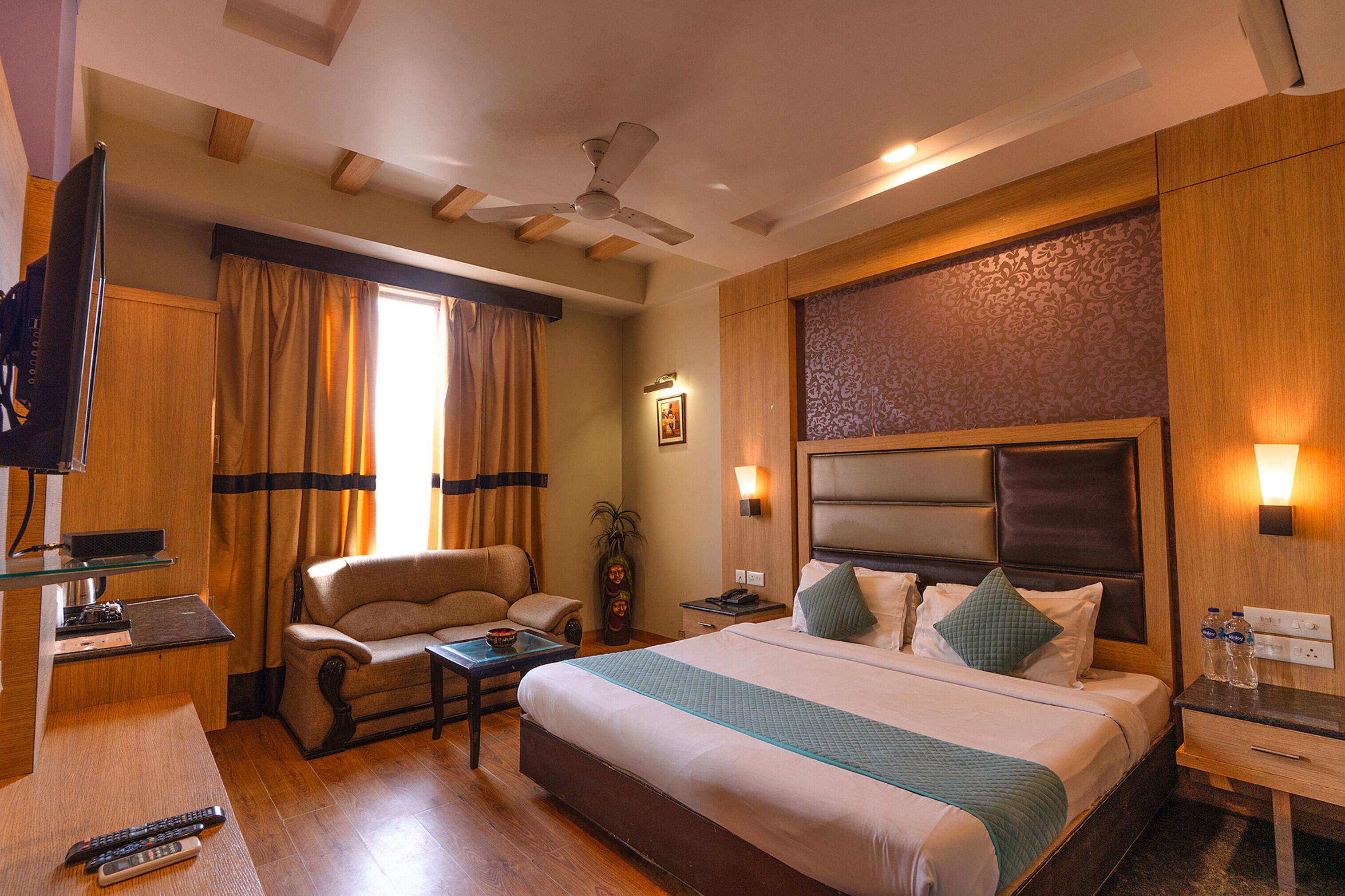 A hotel room with a bed, a desk, a chair, a television, and a ceiling fan.