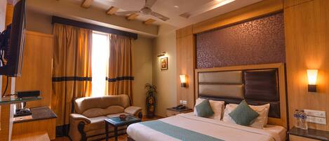 A hotel room with a bed, a desk, a chair, a television, and a ceiling fan.