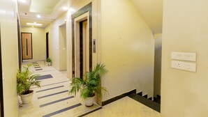 A hallway with potted plants, a marble floor, and an elevator. - Fabhotel Prime Aroma Residency (Jaipur)