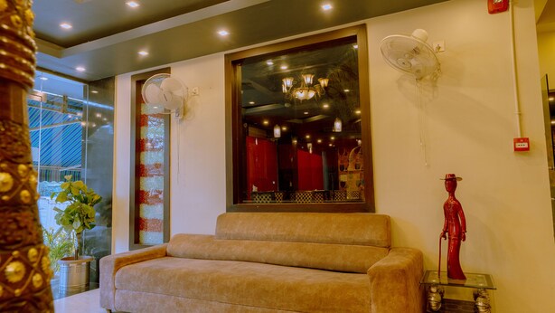 A room with a beige sofa, a glass table with a statue, and a large mirror reflecting a red interior. - Fabhotel Prime Aroma Residency (Jaipur)
