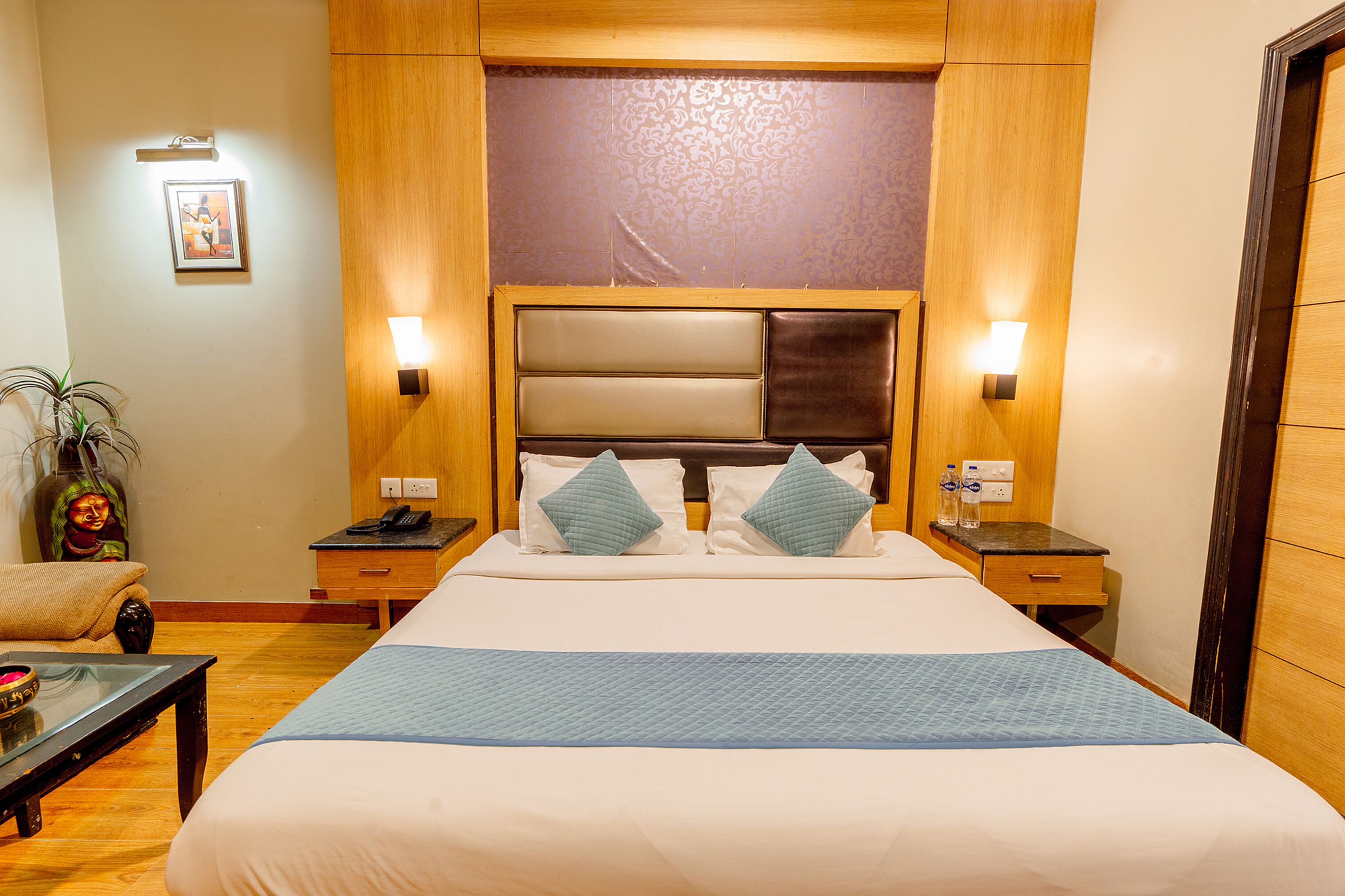 Quarto de hotel com uma cama grande, duas mesas de cabeceira, um criado-mudo, uma cadeira e um quadro pendurado na parede.