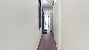 A long, narrow hallway with white walls and a brown floor, leading to a bright area at the end. - Fabhotel Park View I (Manali)