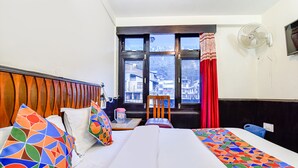 A hotel room with a bed, a chair, a window with curtains, and a wall-mounted fan. - Fabhotel Park View I (Manali)