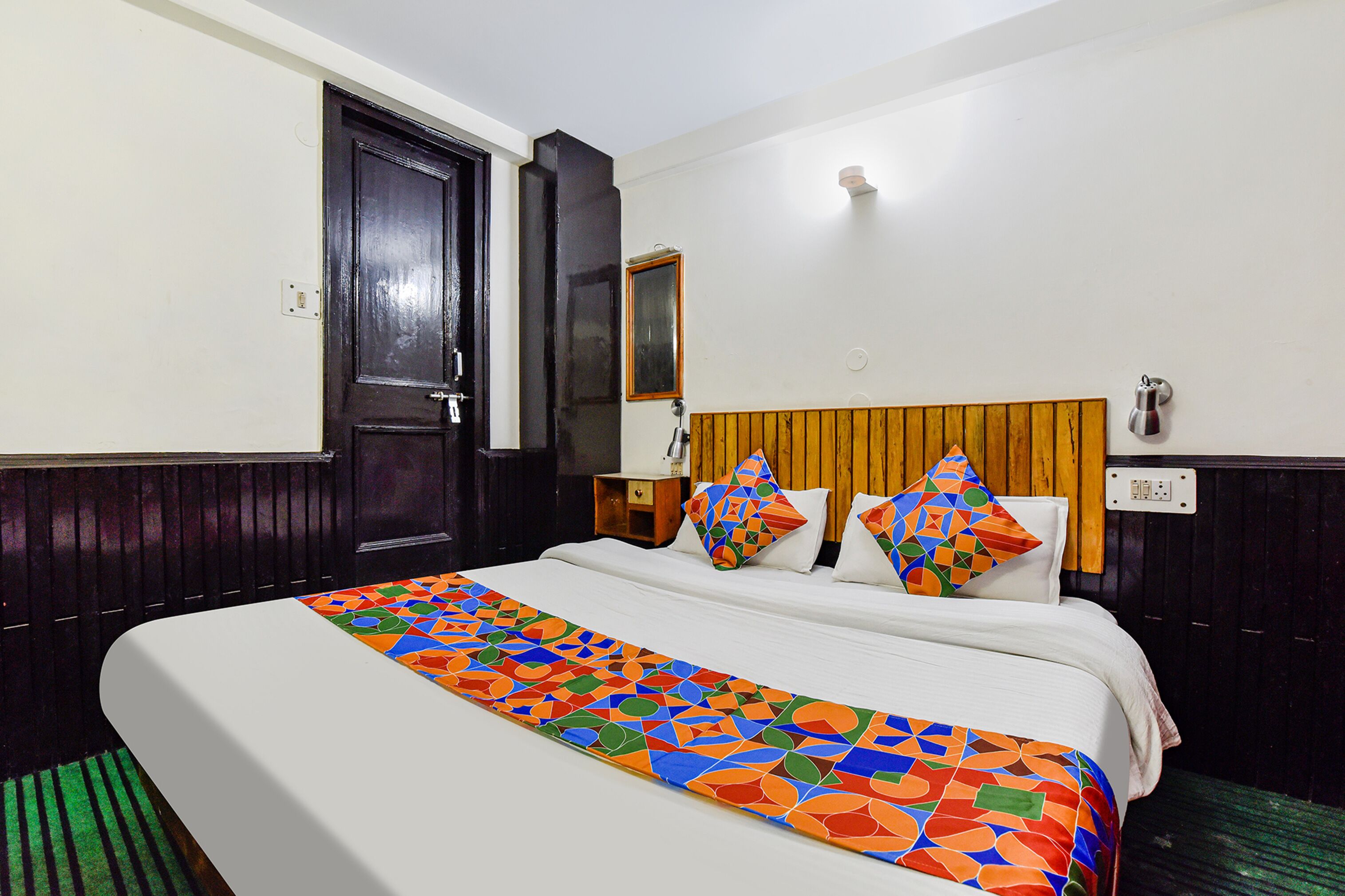 A hotel room with a bed, a nightstand, a mirror, and a door.