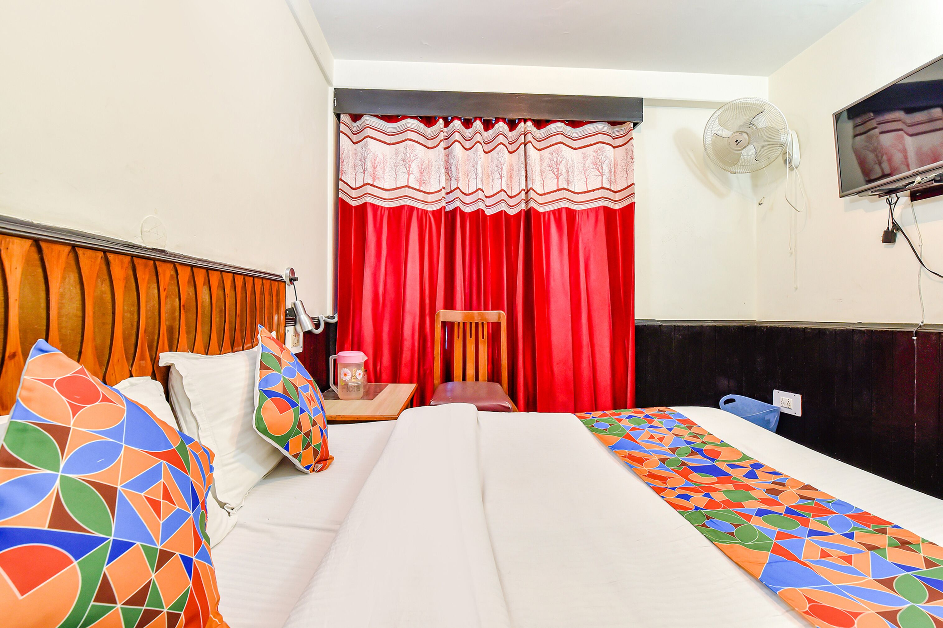 Ein Hotelzimmer mit Bett, Schreibtisch, Stuhl, Ventilator und Fernseher.
