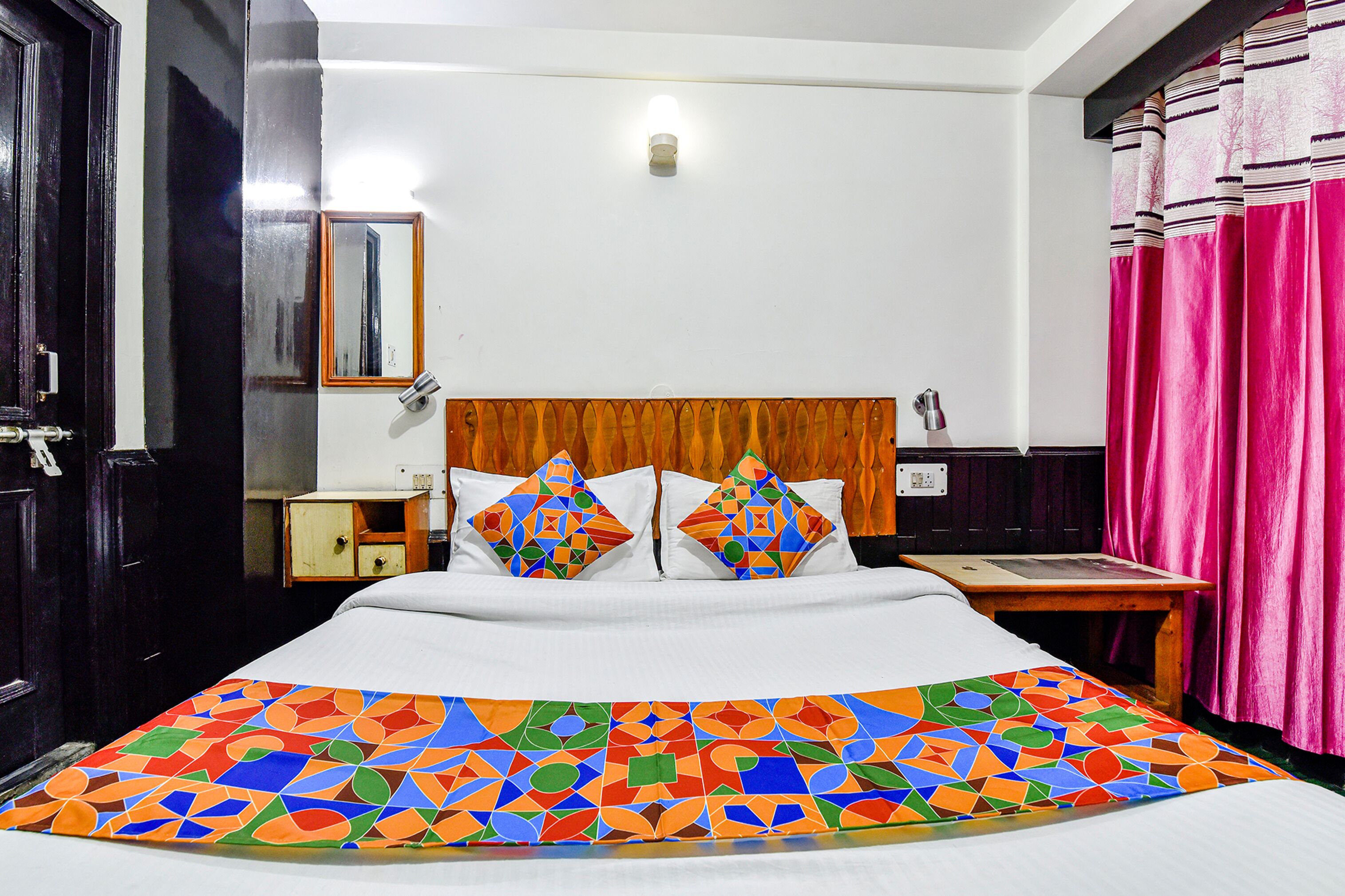 A hotel room with a bed, a nightstand, a mirror, and a window with curtains.