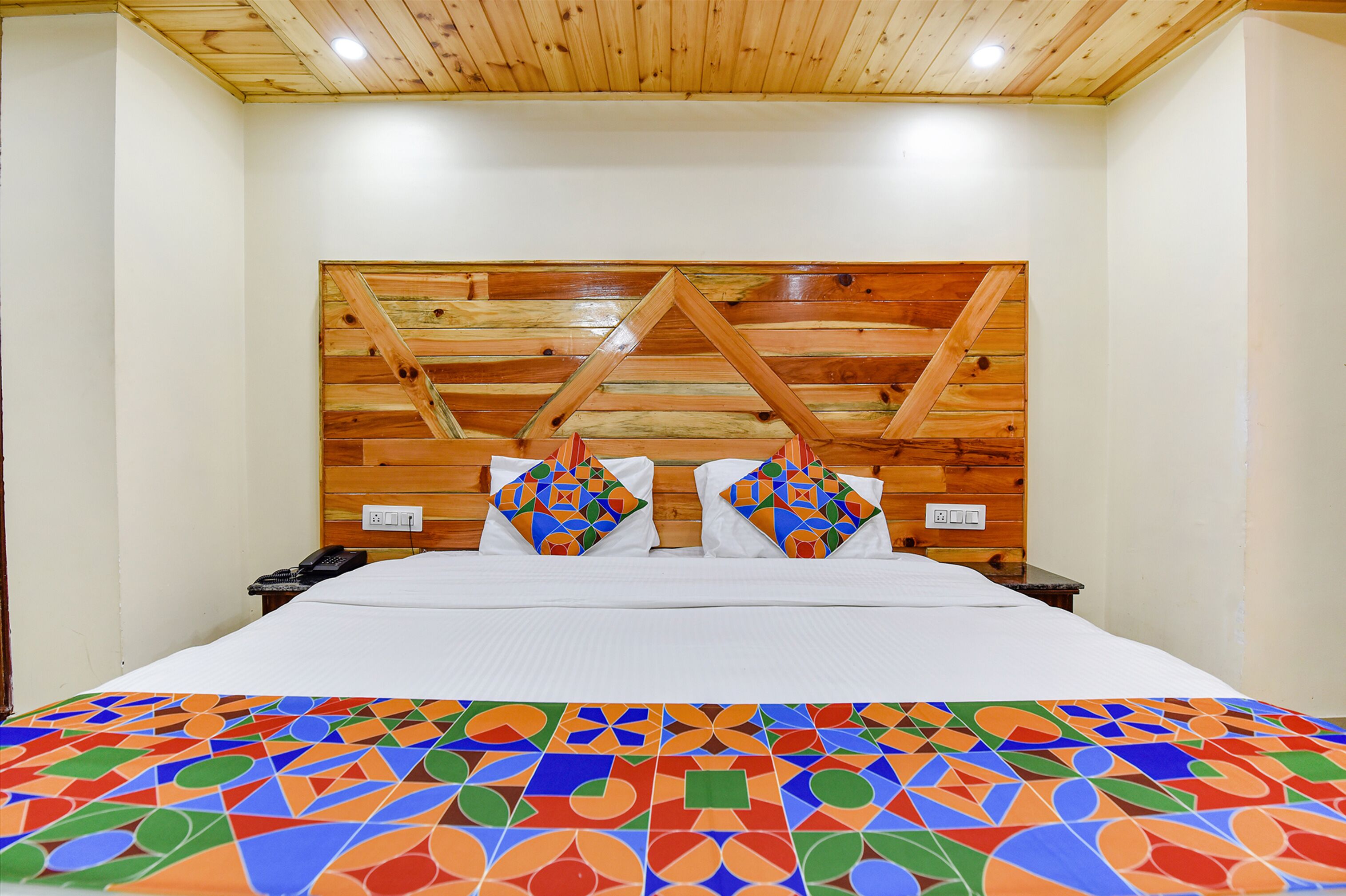 Una cama con una colcha de estampado geométrico, un cabecero de madera y dos mesitas de noche con lámparas.