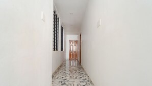 A hallway with a marble floor, white walls, and a wooden door at the end. - Fabexpress Anmol'S Peace Home Stay (Ootacamund)